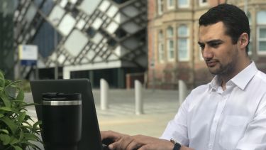 Photo of masters student Sammy Shaw working on a computer outside