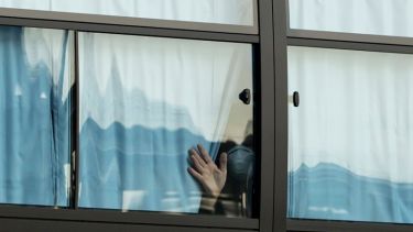 Person in a mask looks out of a window