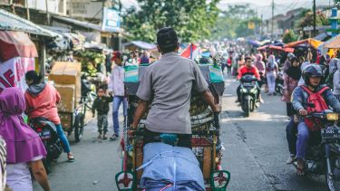 Man riding bike carrying goods through busy market