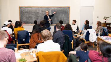 A lecturer stood at the front of a seminar by a blackboard