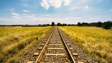 Railroad Track Amidst Grassy Field Against Cloudy Sky
