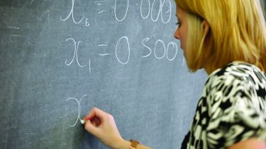 A maths student writing equations on a blackboard