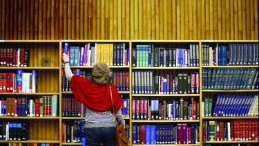 A person taking a book off a high shelf