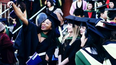 A group of female students in caps and gowns taking a selfie on graduation day.