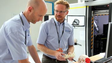 Two men discuss research. One holds a prosthetic bone