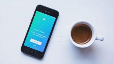 A smartphone with Twitter open next to a cup of coffee