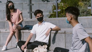 Students sitting on tiled steps chatting while wearing protective masks