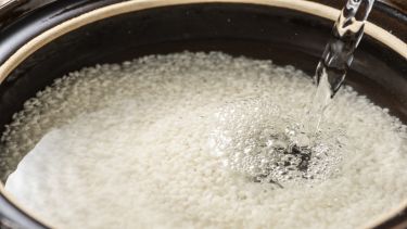 Rice in a pan submerged in water with more water being poured onto it.