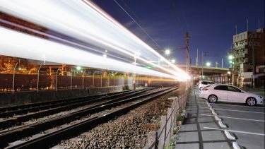 A train flashes past a car park with two white cars