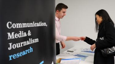 A delegate is welcomed at a conference with the Communication, Media and Journalism research group