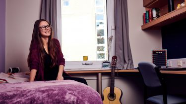 Girl sat on purple bed next to a guitar