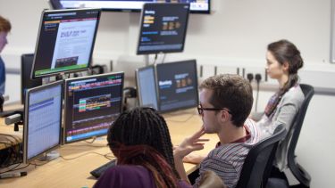 Three students working at terminals running Bloomberg softare