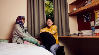 two students sat in a bedroom talking and laughing