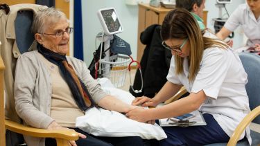 Female nurse helps elderly lady in chair