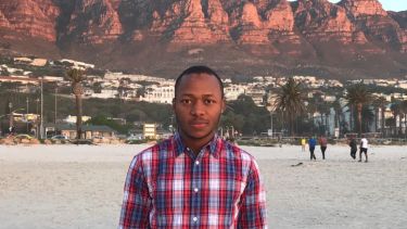 A profile photo of alumni, Saleh. He is wearing a plaid shirt and standing in front of some red rocks. 