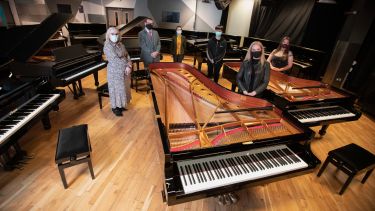 Music department staff and students standing around pianos 