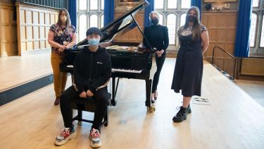 Students stood around a model D piano