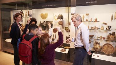 An image of a group of school children in a museum with their teacher, a member of staff from the museum is asking the children questions,
