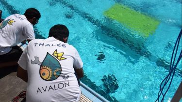 Two people working with the robot at the side of the water.