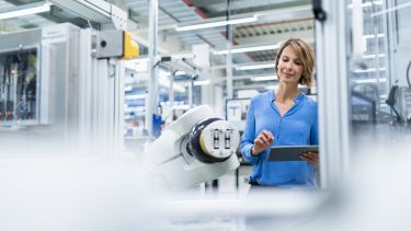 A woman holding a tablet looking at a robot on an assembly line
