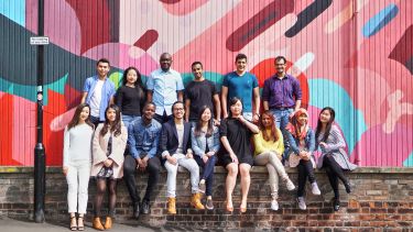 International students sit on a group in front of a brightly decorated wall