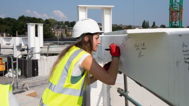 Evie Croxford, SU president, signs some of the steelwork at the Faculty of Social Sciences topping out