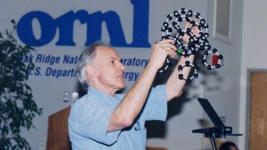 Sir Harry Kroto lecturing, holding up a C60 model