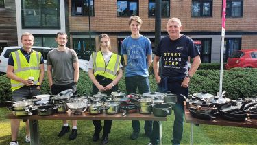 students and member of staff stood in front of a table with pots and pans