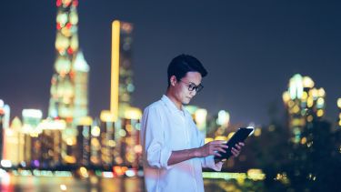 A person holding an iPad in front of skyscrapers