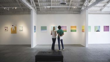 Two people looking at paintings in an art gallery