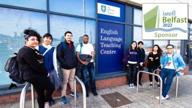 A group of 8 students stood outside the entrance to the ELTC building, with the IATEFL Belfast 2022 conference logo in the top right corner.