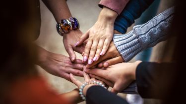 A photo of a circle of people putting their hands into the centre of the circle.