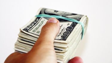 A wad of cash, wrapped in a rubber band, in a person's hand