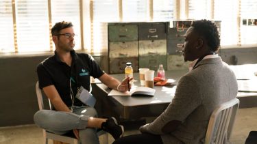 A image of a white male and a black male sat opposite each other having a 1 to 1 meeting