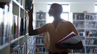 A young man removing a book from shelf in library