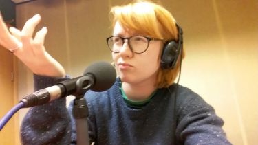 Woman sat at radio mic with headphones raising hand palm up