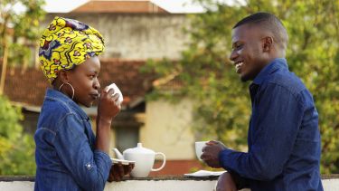 A photograph of a male and female Ugandan talking and sharing a pot of tea.