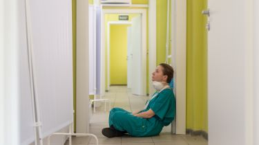 Woman sat on the floor in scrubs, mask round her neck