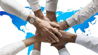 Several hands put into the centre of a circle. The image background is a map of the world.