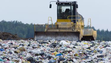 A photograph of a large digger driving through a landfill site