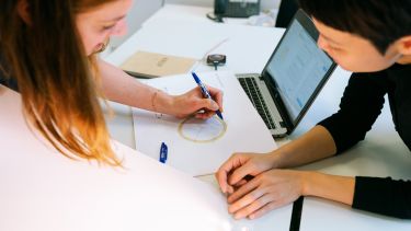 Woman discusses with colleague whilst annotating diagram