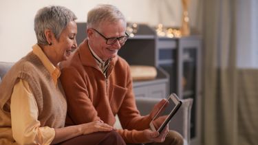 An elderly couple sat on a sofa using a tablet together.