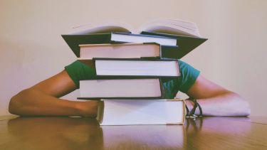 A photo of a person with their head down in a pile of books