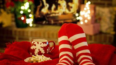 A photograph of stripy socks and a snowflake mug in front of a lit fireplace. 