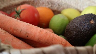 A basket of fruit and vegetables, including carrots, tomatoes, oranges, limes and avocado