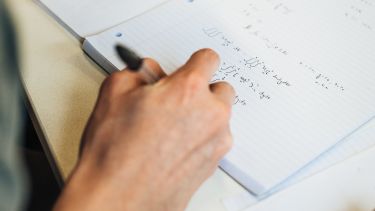 Photo of a hand writing mathematical terms in a workbook