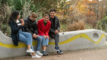four students sat on a wall laughing together