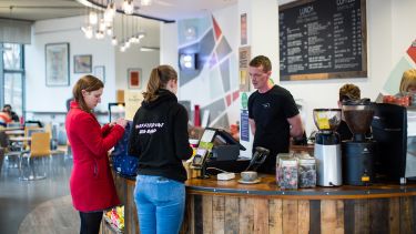 two women stood at a coffee counter while a man waits to serve them