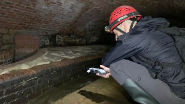 Man crouched down recording water in cave 