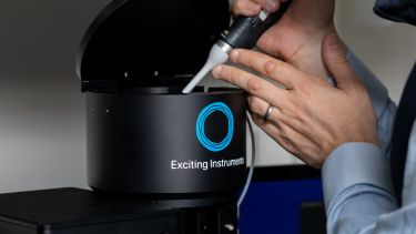 Image of the inside of the EI-FLEX System, a black benchtop instrument, being measured with a tool